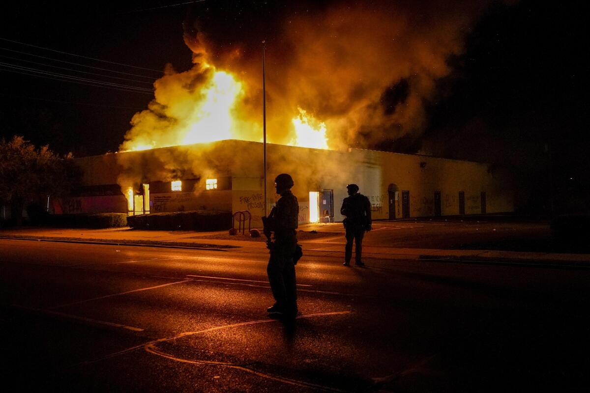 Police stand near a Department of Corrections building set ablaze during protests in Kenosha, Wis.