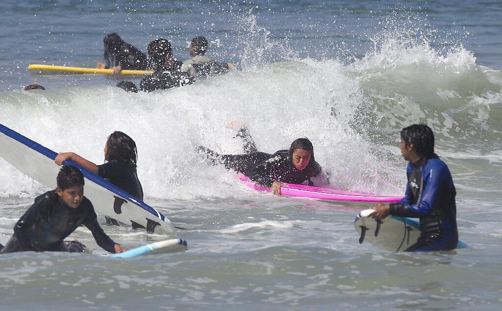 Surfer Jackie Olivares, on pink board, hangs on tight to her board during Save Our Youth’s Surf Days program in west Newport on Thursday.