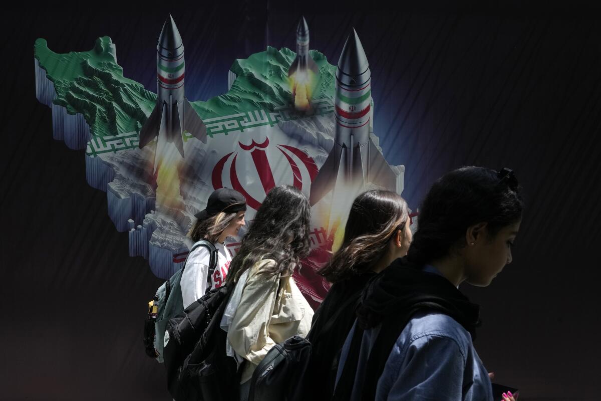 Women in Tehran on Friday walk past a banner showing missiles being launched from an Iranian map.