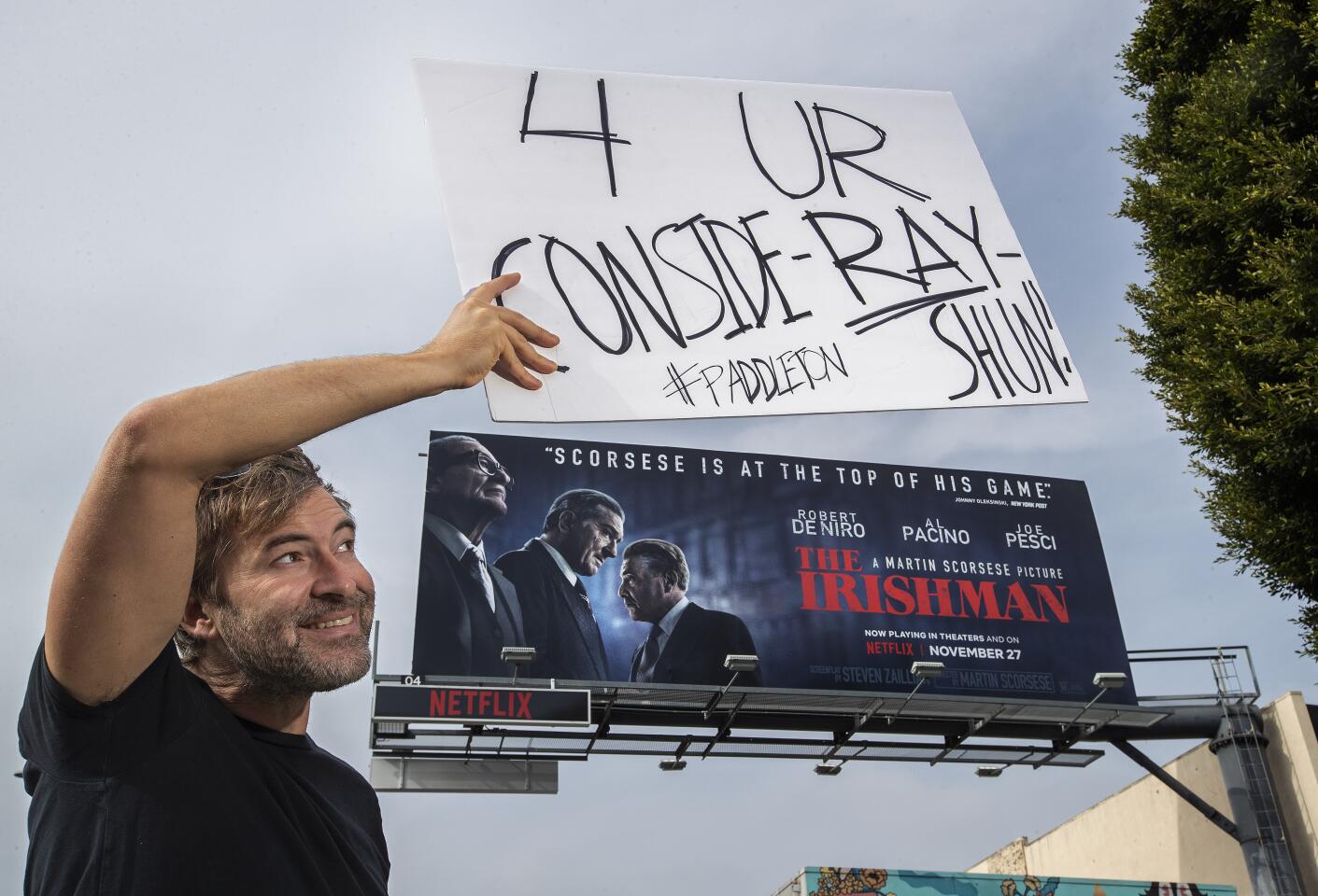 LOS ANGELES, CA-NOVEMBER 15, 2019: Actor Mark Duplass holds a sign above a billboard on Sunset Blvd, along the Sunset Strip in Los Angeles, promoting the movie, The Irishman, as he conducts a one-man awards campaign for his “Paddleton” co-star Ray Romano on November 15, 2019. Romano appeared in The Irishman. (Mel Melcon/Los Angeles Times)