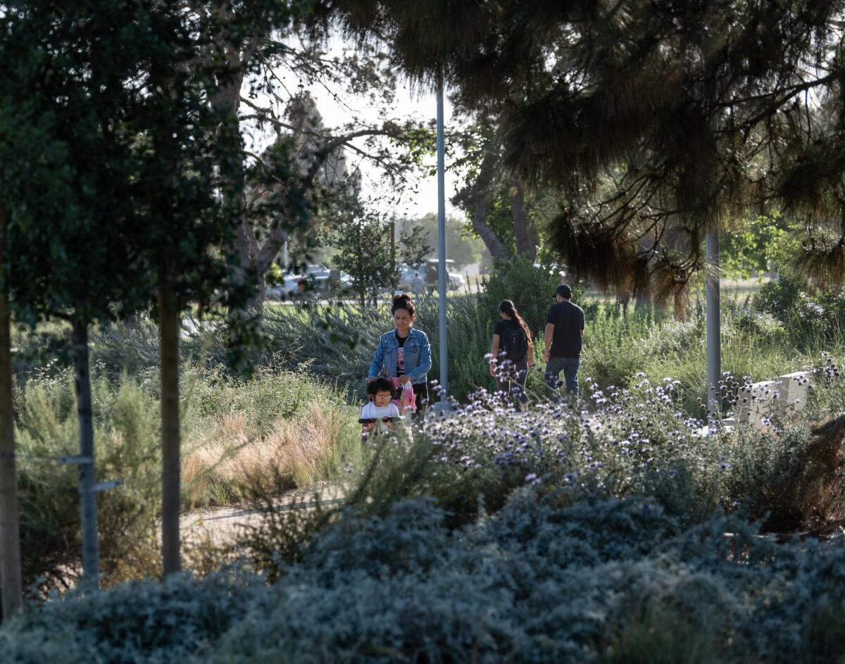 A woman and child walks through a tree-lined section of Magic Johnson Park filled with plants in bloom