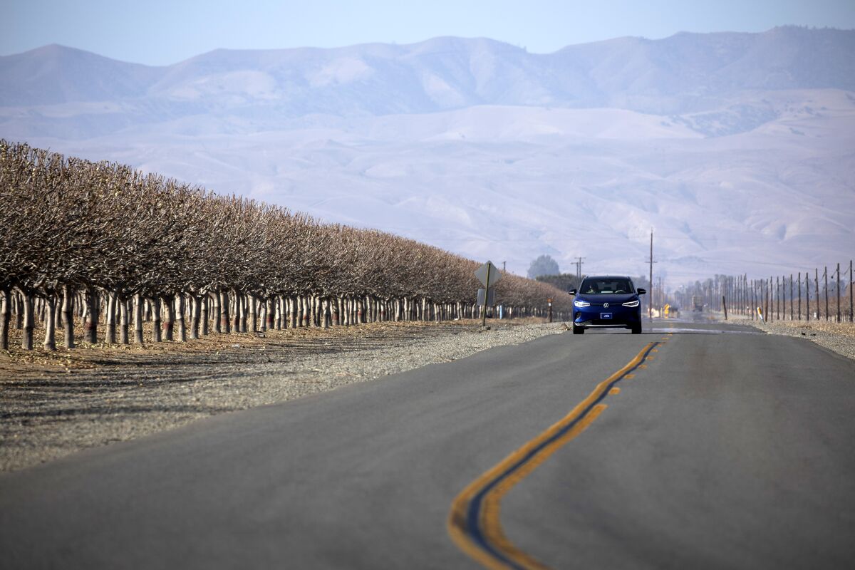 An electric VW drives on a road past a grove in Huron, Calif.