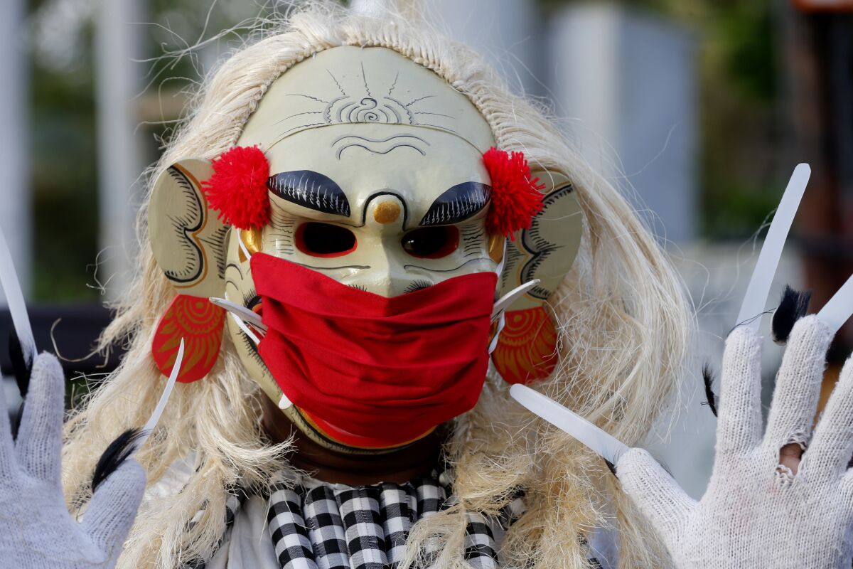 A man wearing a traditional Balinese celuluk costume with a face mask as a precaution against the coronavirus during a campaign to keep on wearing masks in public places in Bali, Indonesia, Saturday, Oct. 3, 2020. (AP Photo/Firdia Lisnawati)