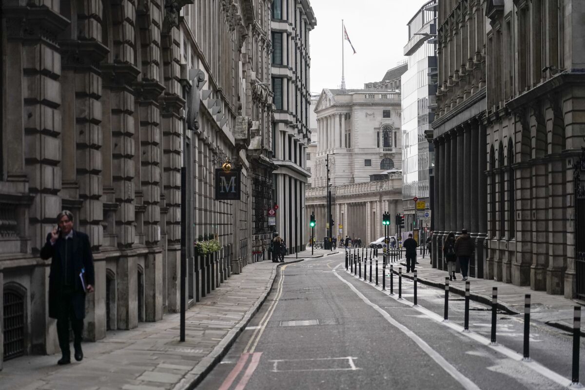 A man talks on the phone while walking in an empty street in the financial district, known as The City, in London, Monday, Dec. 13, 2021. While many people will re-start working from home, the British government raised the country's official coronavirus threat level on Sunday, warning the rapid spread of omicron "adds additional and rapidly increasing risk to the public and health care services" at a time when COVID-19 is already widespread. (AP Photo/Alberto Pezzali)