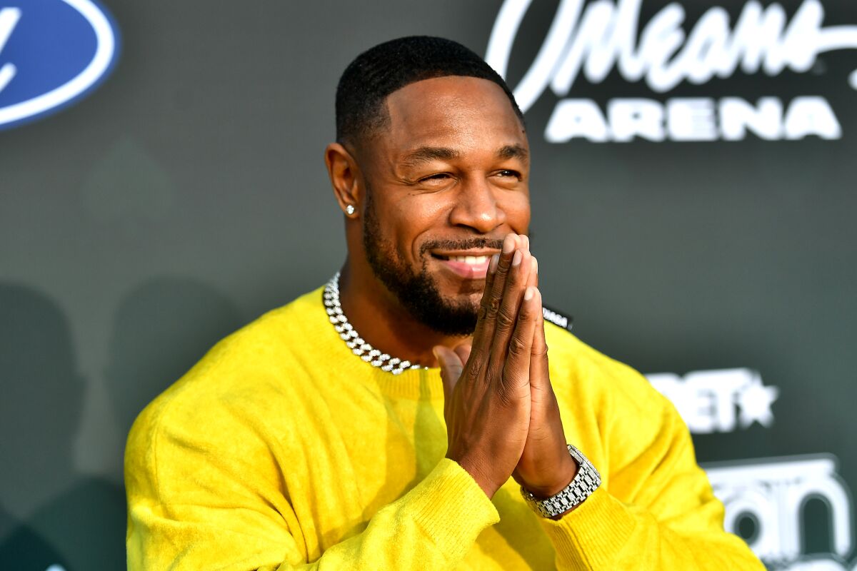 Singer Tank, in a yellow sweatshirt, smiles and presses his palms together