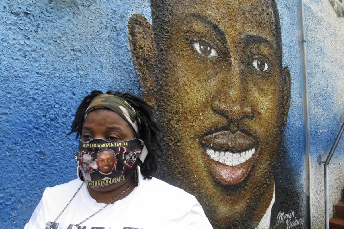 Thea Brooks stands in front of a mural of her slain nephew, Ahmaud Arbery.