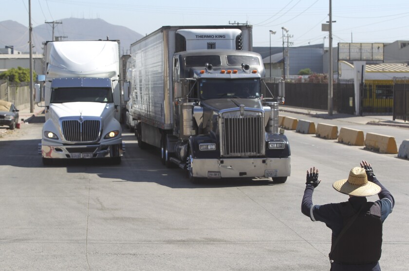 A Tijuana security guard directs commercial trucks as they wait in line to cross at the Otay Mesa Port of Entry 
