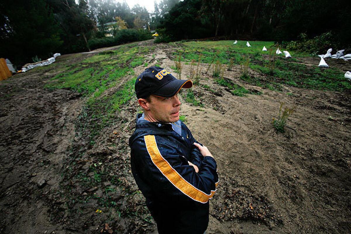 After a rainstorm, Eric Grey stands in a field partially covered by mud and debris behind his home in La Canada Flintridge. He has built a wall and is working on a barricade to help protect his home from possible future mudslides.