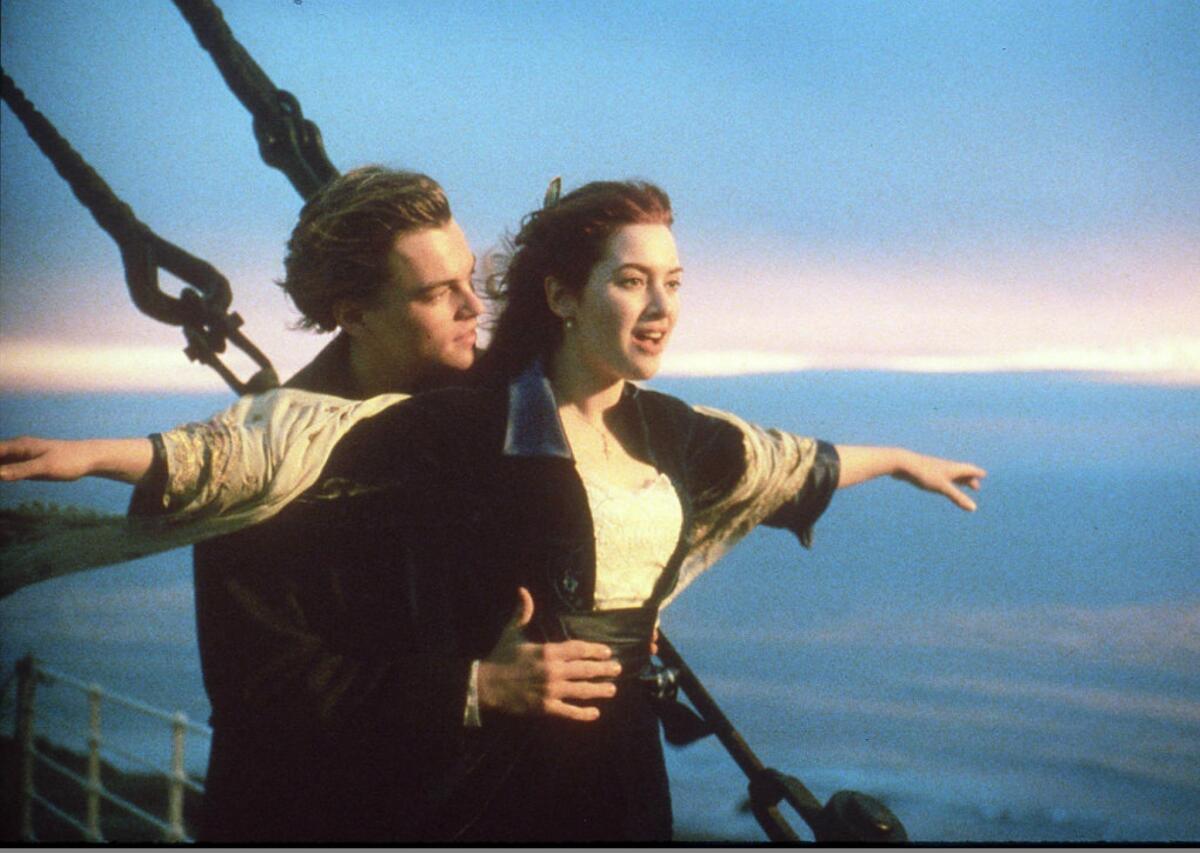 A man placing his hands on the waist of a woman with her arms outstretched on a ship