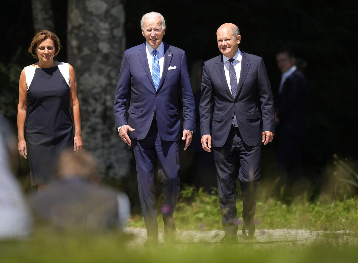 German Chancellor Olaf Scholz and President Biden walk beside a woman.