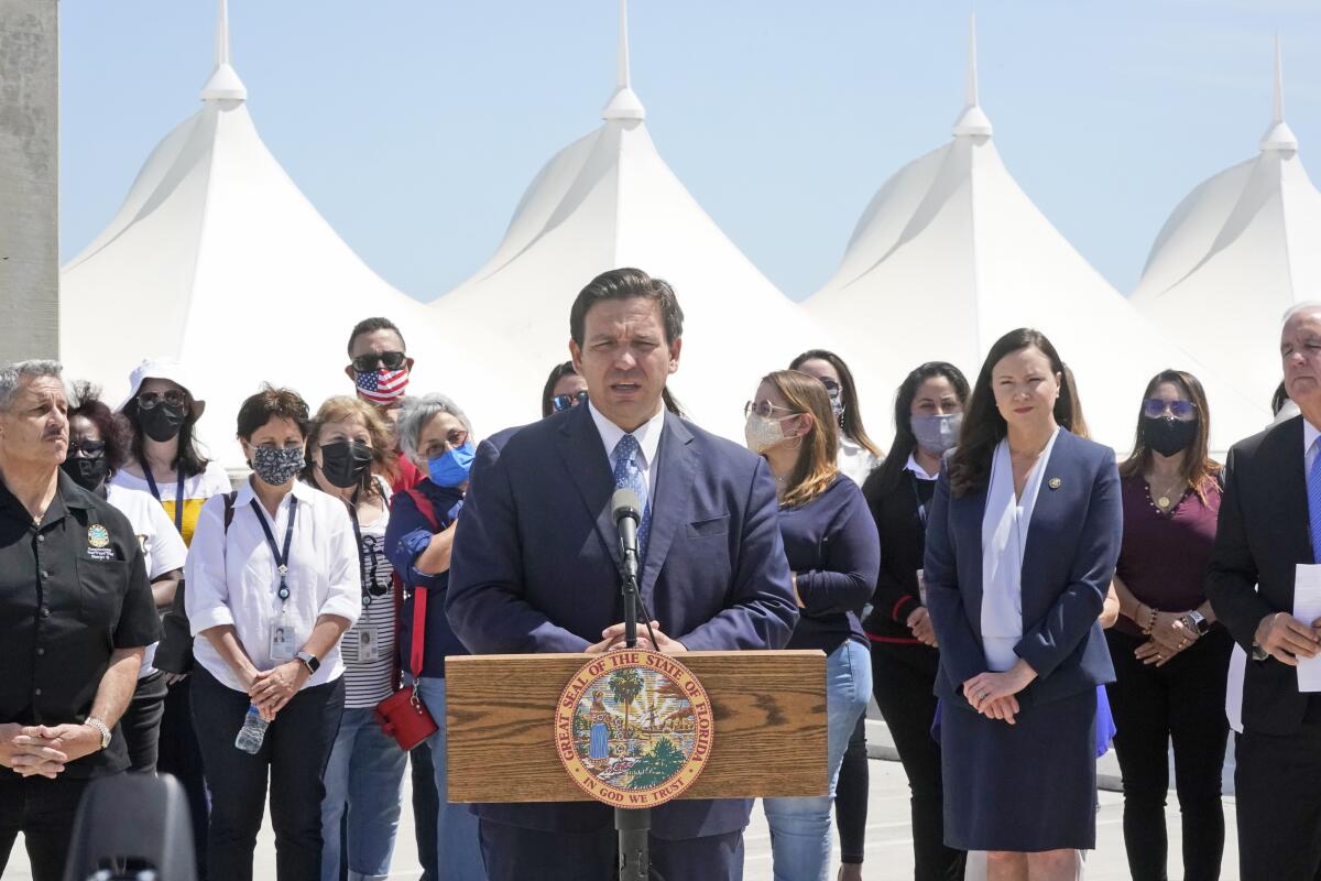 Florida Gov. Ron DeSantis, center, speaks during a news conference surrounded by officials and cruise workers, Thursday, April 8, 2021, at PortMiami in Miami. DeSantis announced a lawsuit against the federal government and the CDC demanding that cruise ships be allowed to sail. (AP Photo/Wilfredo Lee)