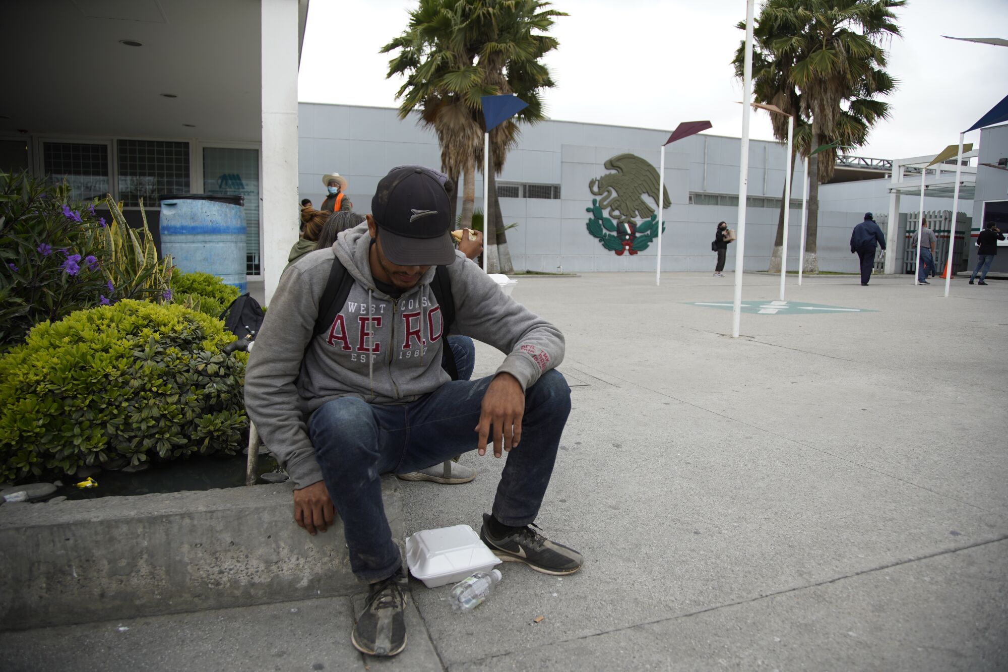 Francisco sits near the pedestrian border crossing to eat lunch from a foam container at his feet