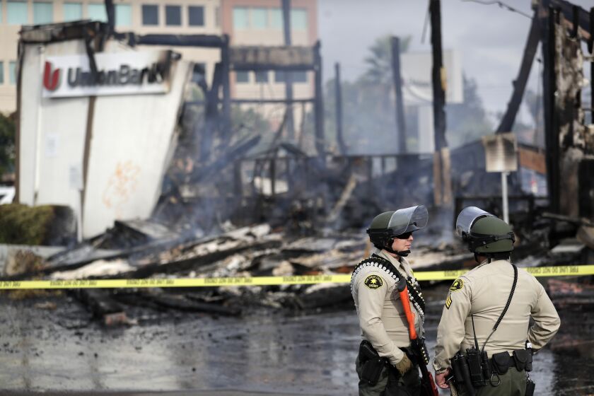 San Diego County sheriff officers stand guard in front of a burning bank building after a protest over the death of George Floyd, Sunday, May 31, 2020, in La Mesa, Calif. Protests were held in U.S. cities over the death of Floyd, a black man who died after being restrained by Minneapolis police officers on May 25. (AP Photo/Gregory Bull)