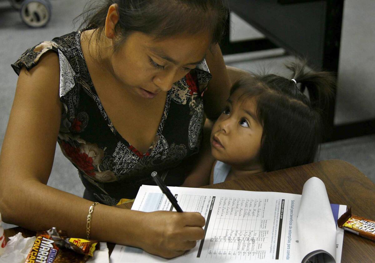 Gabriella Munoz of Orange fills out an application for food stamps while her 2-year-old daughter vies for her attention in October 2006.