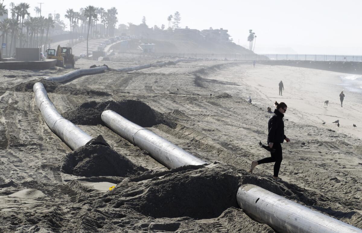 A beachgoer crosses dredging pipe on the beach in Carlsbad just south of Tamarack Beach on Friday.