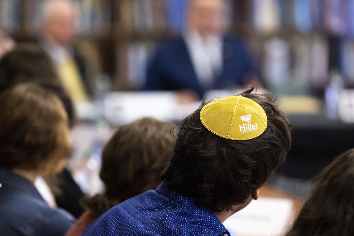 A person among an audience wears a kippah, viewed from behind him. 