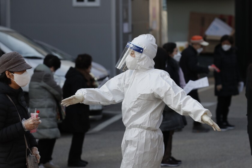 A medical worker wearing protective gear speaks as people wait in queue during testing for COVID-19 at a coronavirus testing center in Seoul, South Korea, Saturday, Dec. 12, 2020. (AP Photo/Lee Jin-man)