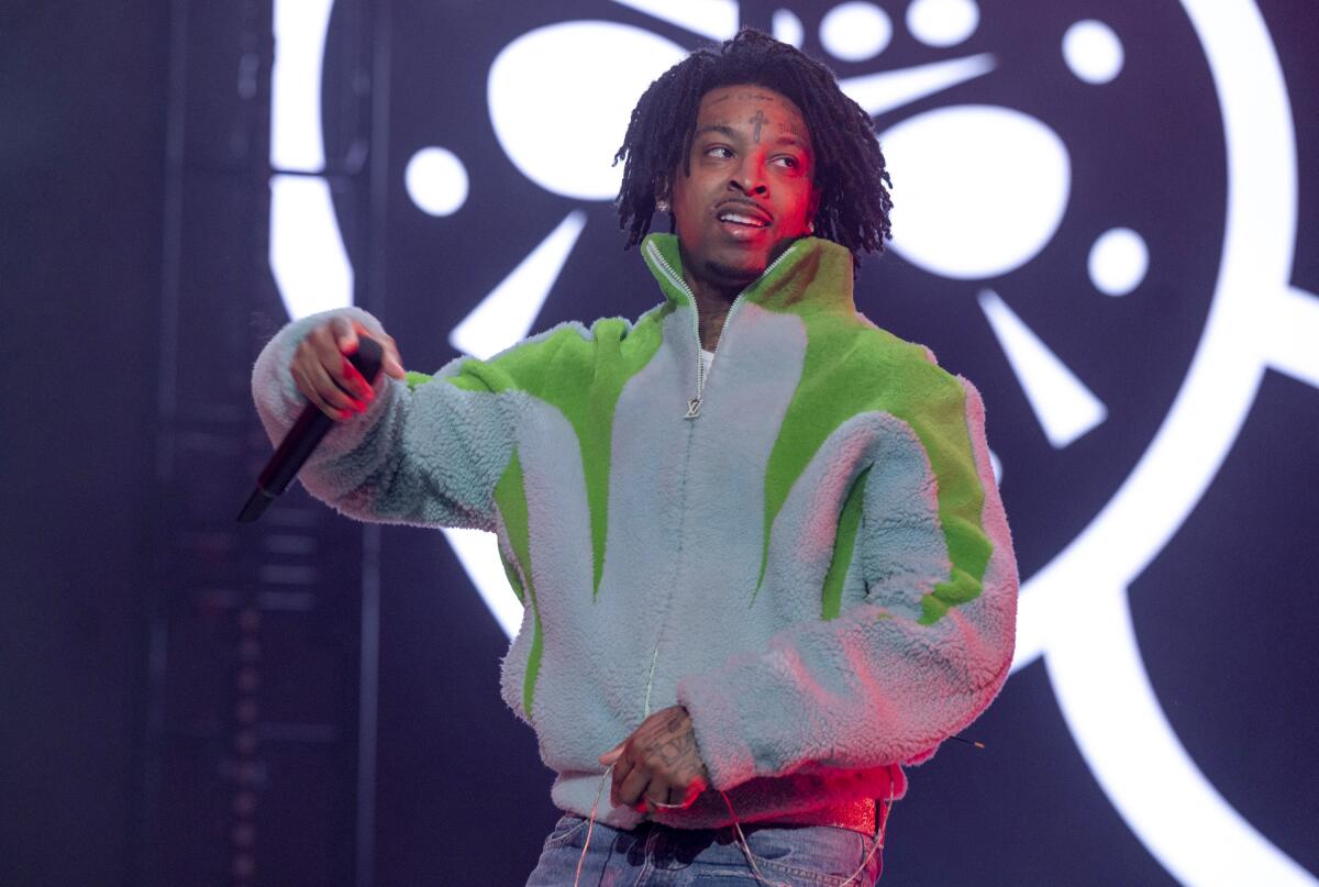 21 Savage wears a blue and green sweater as she performs onstage.