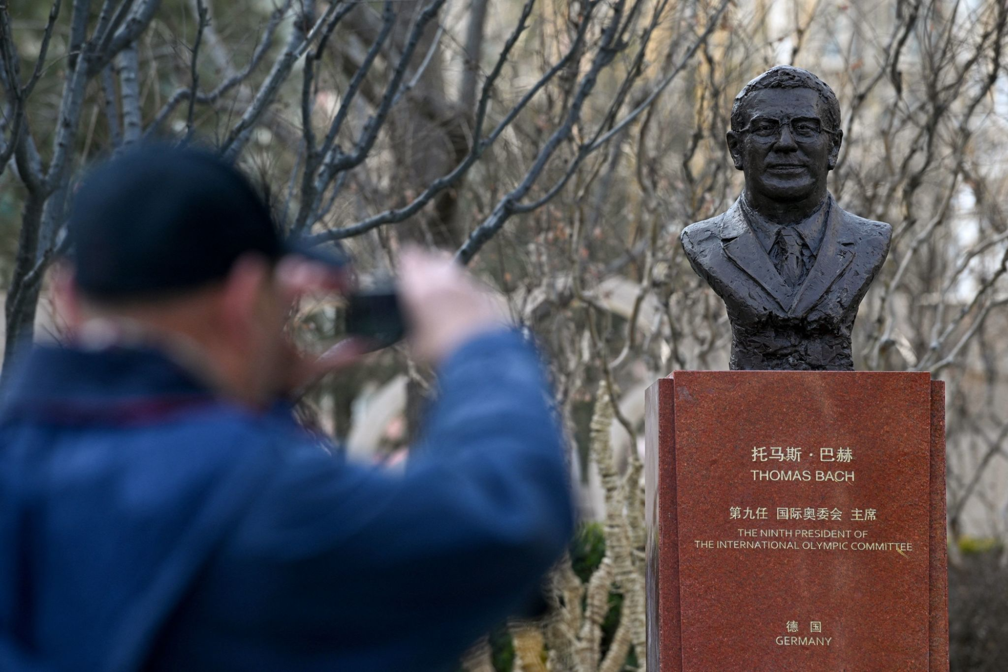 A man takes a photo of a head bust of Thomas Bach.