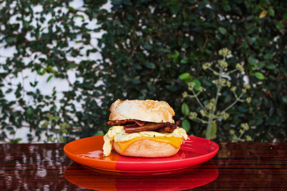 A photo of a bacon, egg and cheese sandwich served on pineapple buns, sitting on an orange and red plate on the patio