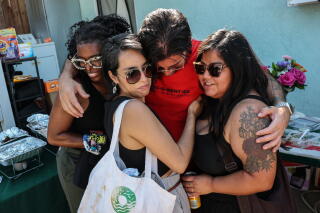Four people wearing glasses, one holding a white tote bag, embrace in a group hug