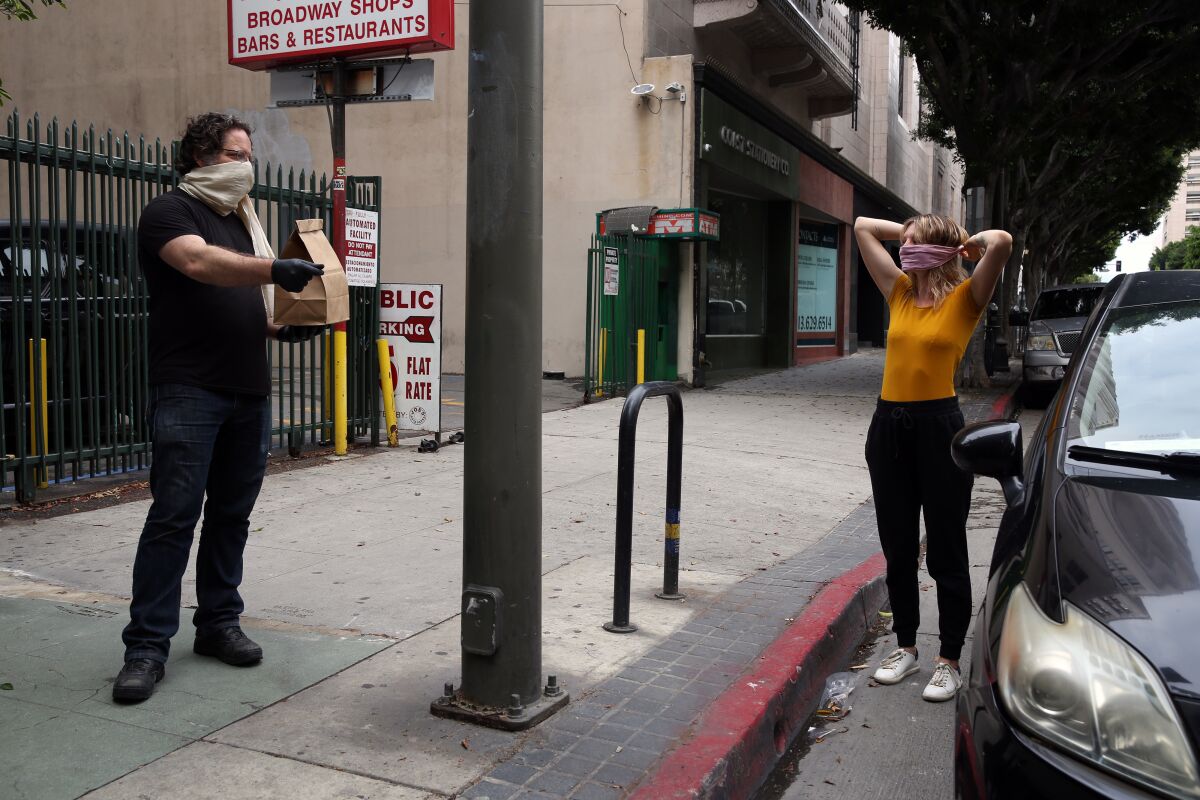 Eric Larkin hands over a pickup order to Brittany Wright as she fastens her mask outside the Last Bookstore in downtown L.A.