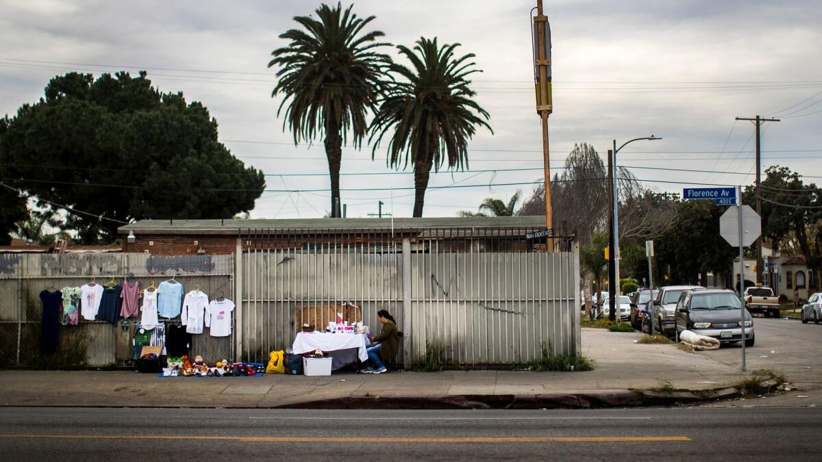 A woman sells her wares in front of a fenced-in lot in the 400 block of East Florence Avenue, where a developer had proposed putting a homeless housing project.