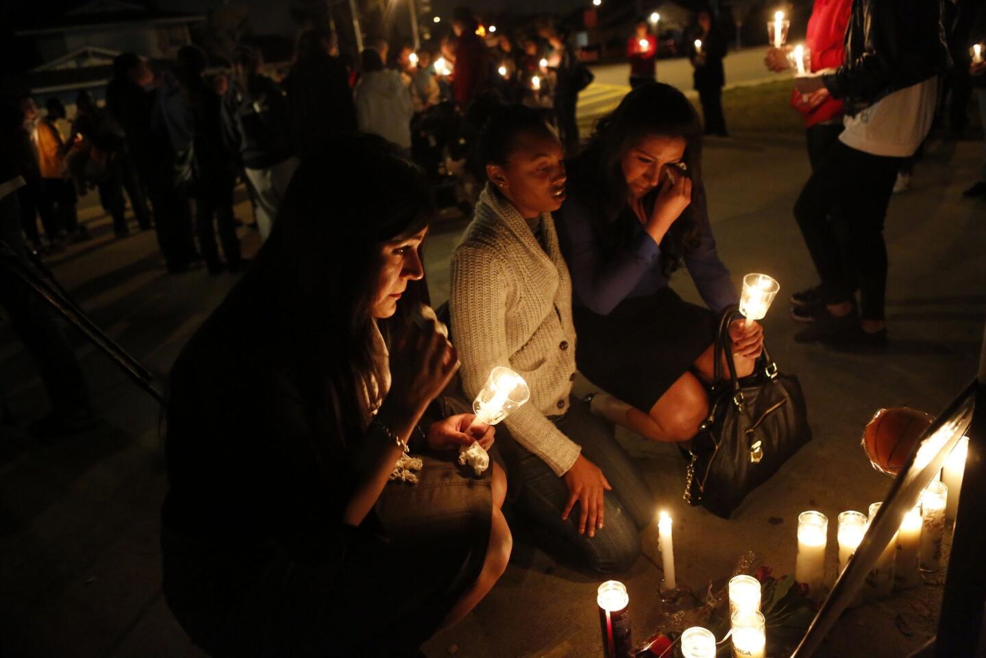 Monica Quan's basketball teammate and friend, Julie Escalera, left, sits with Germita Haynie, center, and Stephanie Escalera as they pay their respects in front of candles and photos of the slain basketball coach.
