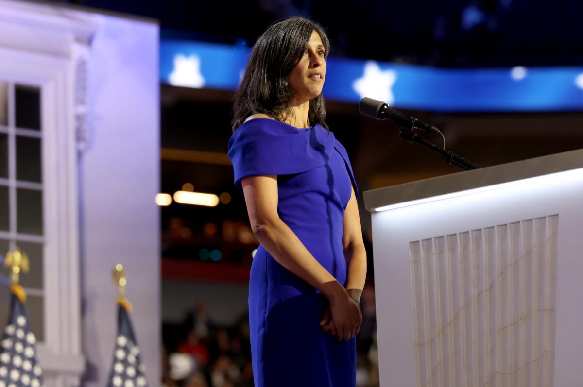 A woman in a deep purple dress stands with hands clasped