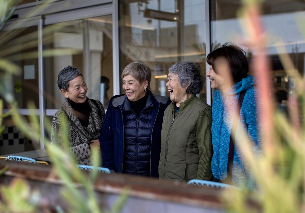Four Japanese mothers stand together laughing