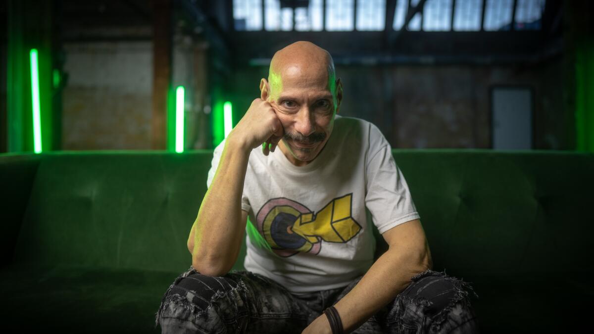 Nicky Siano sitting in a white T-shirt and dark pants with his hand against his cheek.