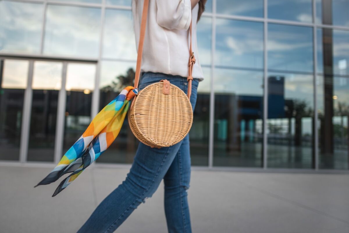 A person carries a round wicker purse with colorful scarf.