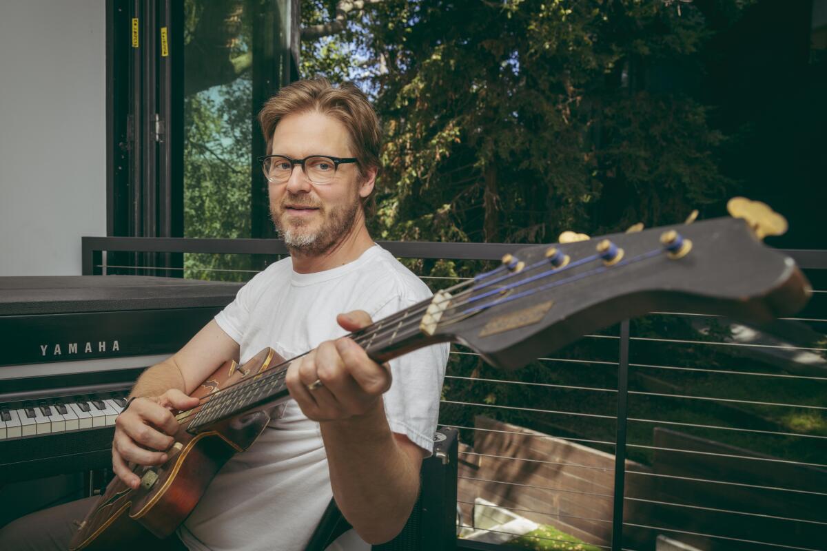 Man in glasses holding a bass while sitting at a piano