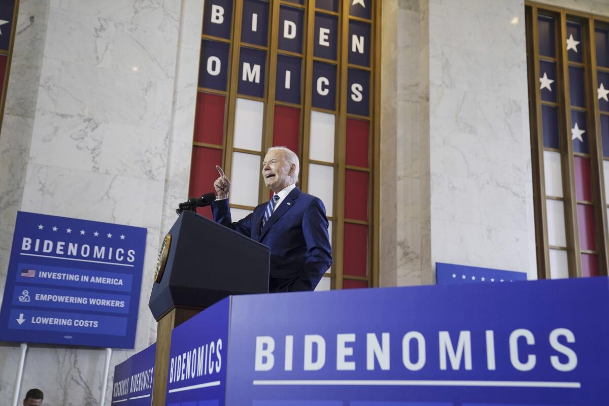 President Biden speaks at a lectern surrounded by signs that say Bidenomics.