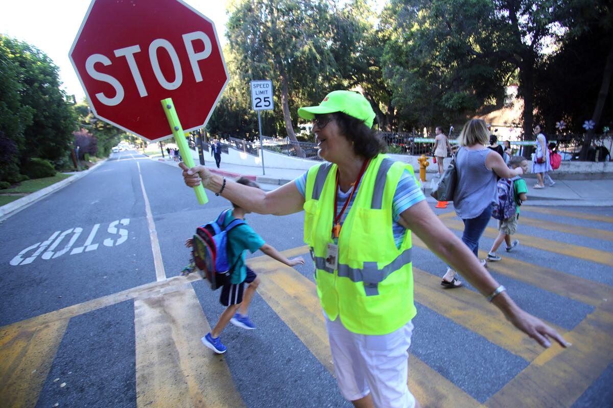 Evelyn Harris, the crossing guard stationed near Palm Crest Elementary School, stops traffic for students as they cross the street on the first day of school.