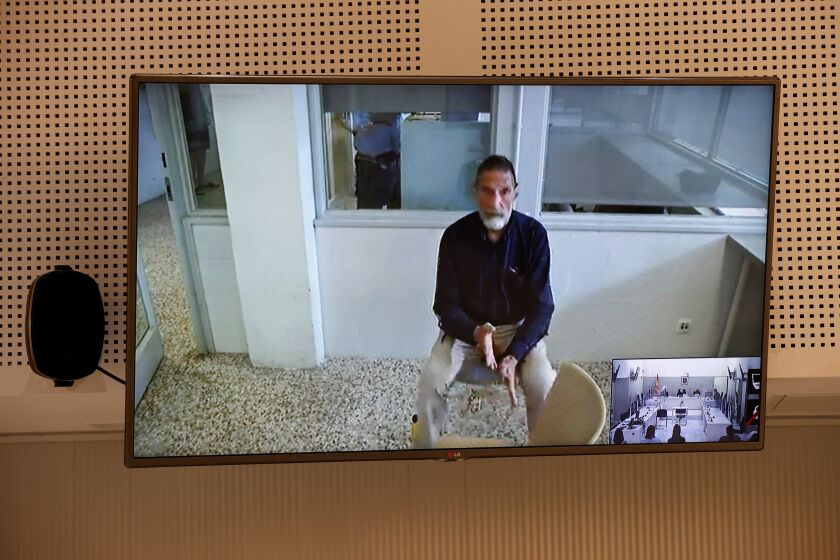 John McAfee, creator of McAfee antivirus software is seen on a screen while testifying via video during an extradition hearing at the National Court in Madrid, Spain, on June 15, 2021. McAfee has been found dead on Wednesday June 24, 2021, in his jail cell near Barcelona in an apparent suicide, hours after a Spanish court approved his extradition to the United States to face tax charges which may have been punishable by decades in prison. Inset photo bottom right is a view of the courtroom. (Chema Moya, Pool photo via AP)