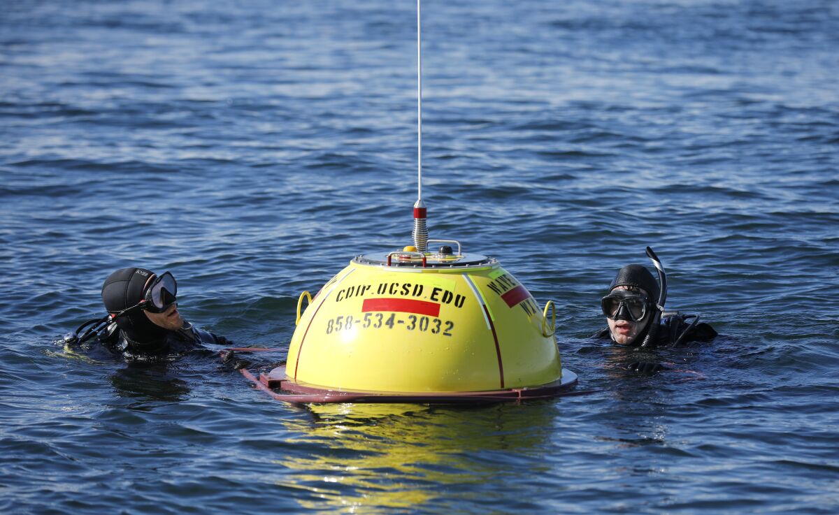 Les Hanson, left, and Jim Behrens of the Coastal Data Information Program make final adjustments on a wave buoy off the coast of Del Mar on Dec. 5, 2019. The buoy measures wave heights and current patterns near the area where bluffs have collapsed.