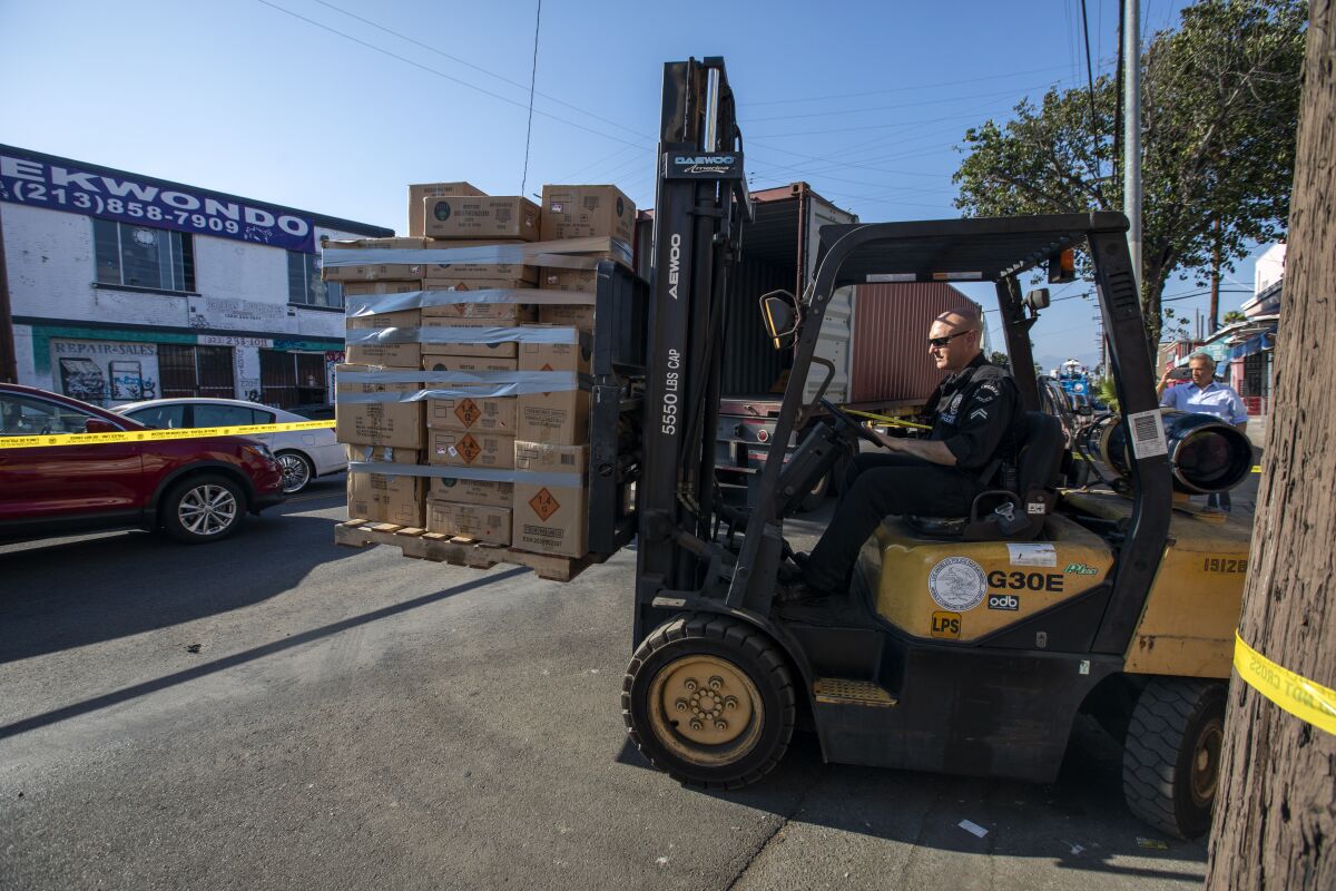 A person in uniform drives a forklift loaded with a pallet of boxes. 