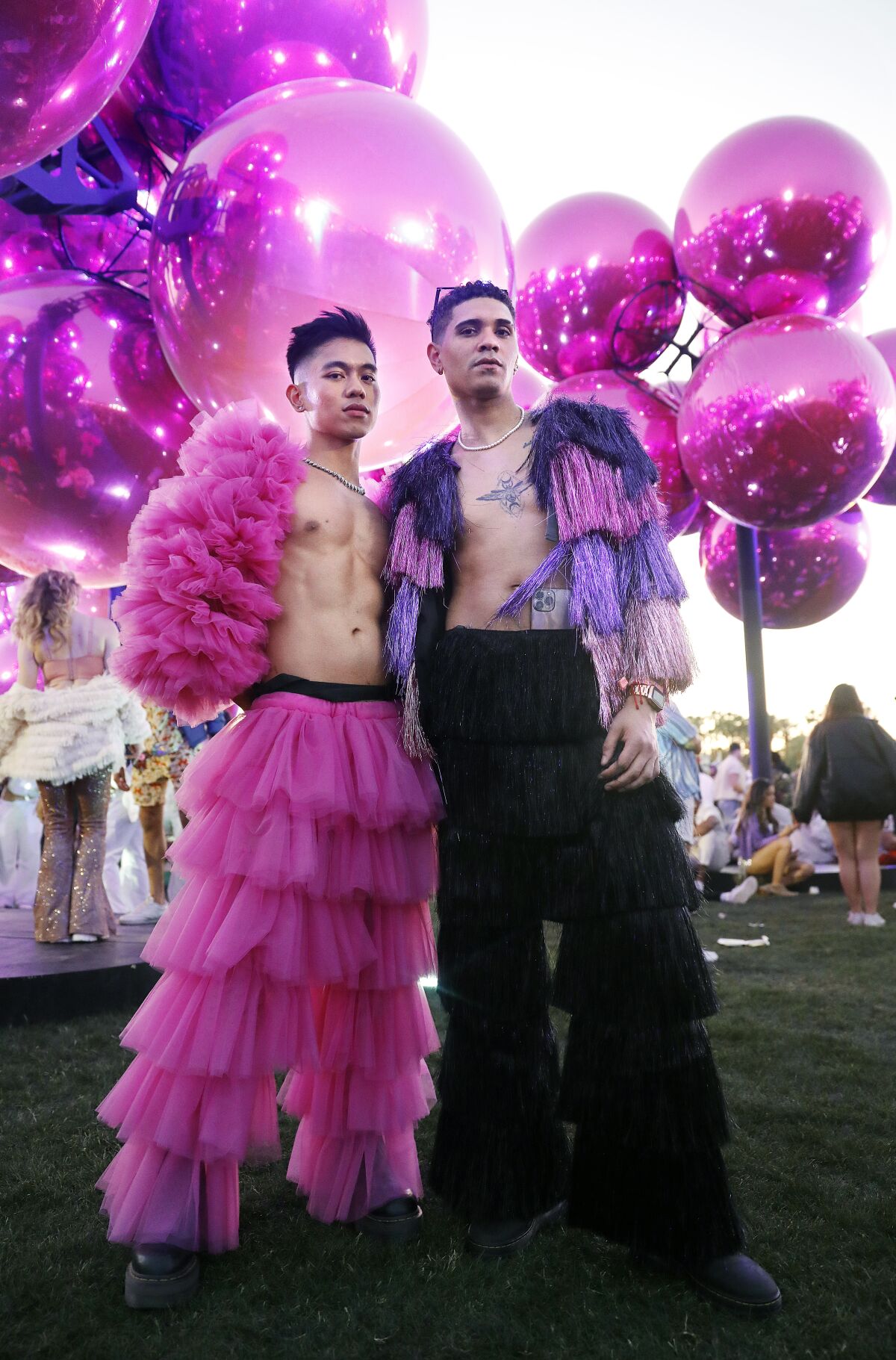 Two people pose for a fashion portrait in front of a sculpture of pink globes 