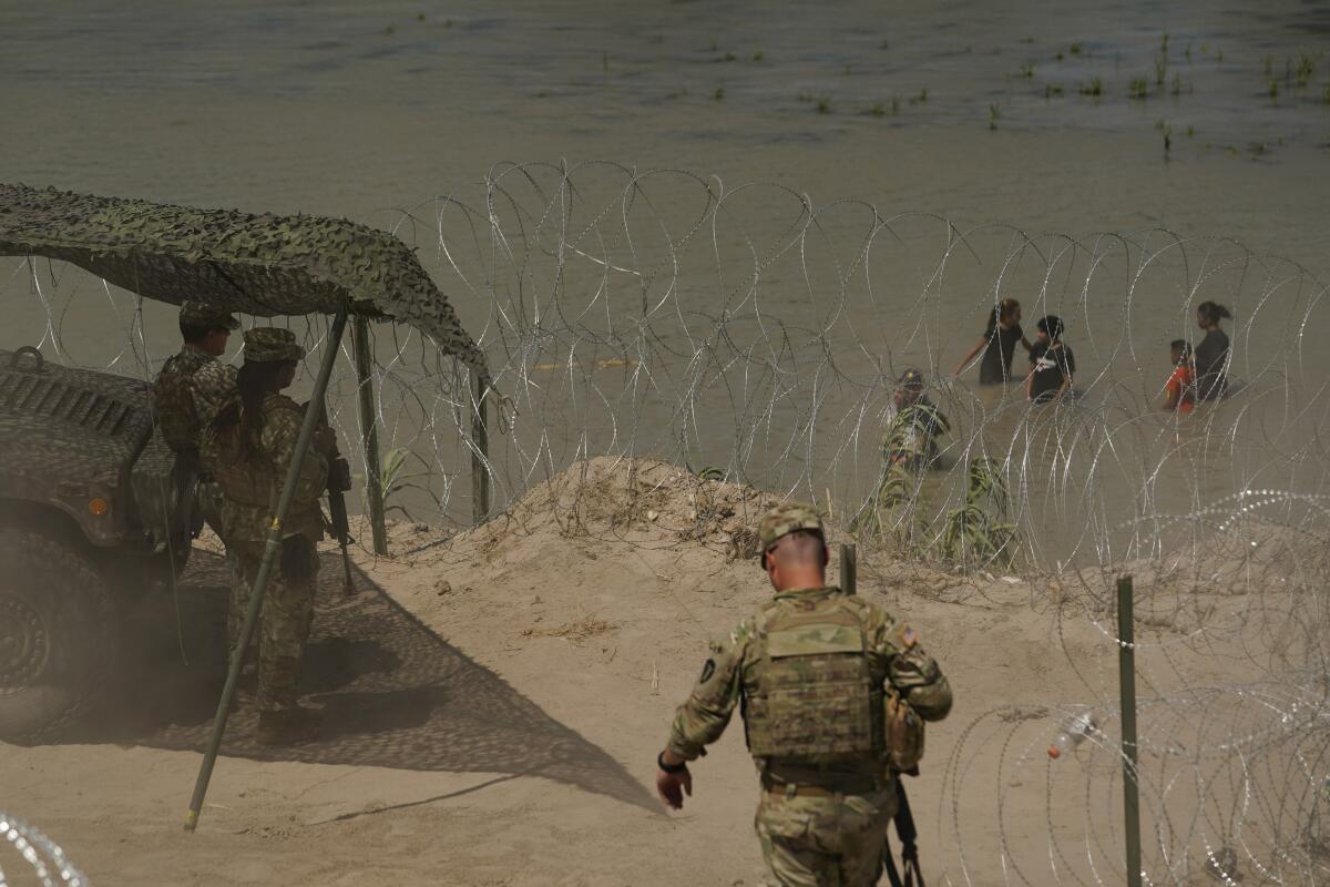 Armed men in fatigues above a riverbank with concertina wire