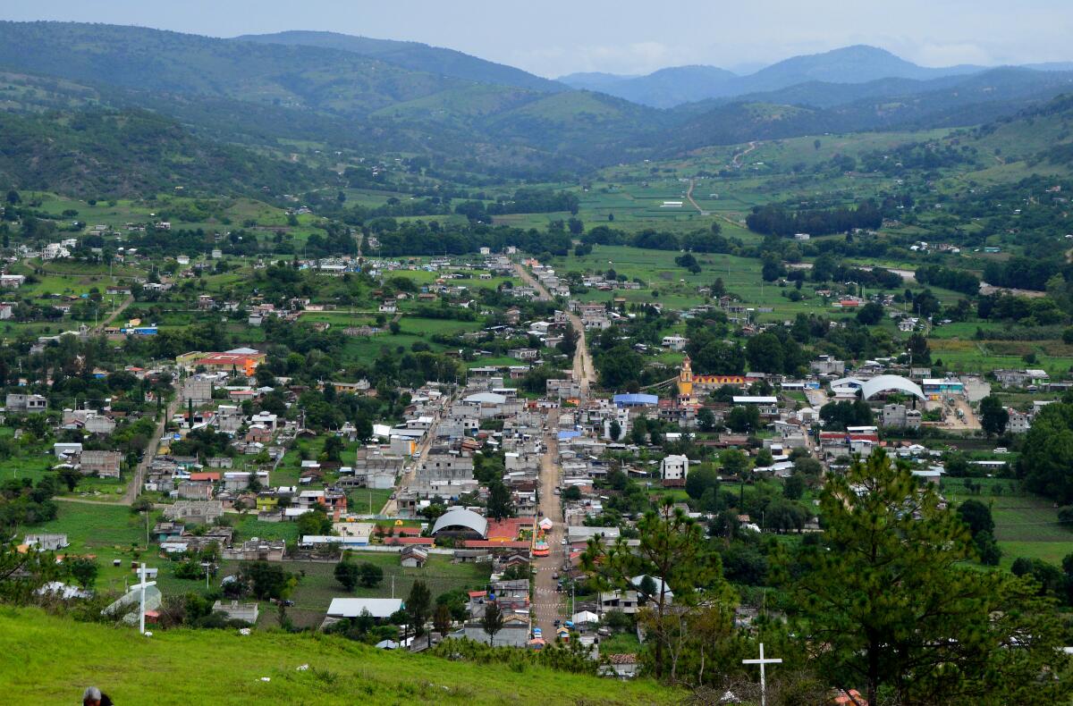 Buildings in a valley surrounded by green fields and mountains. 