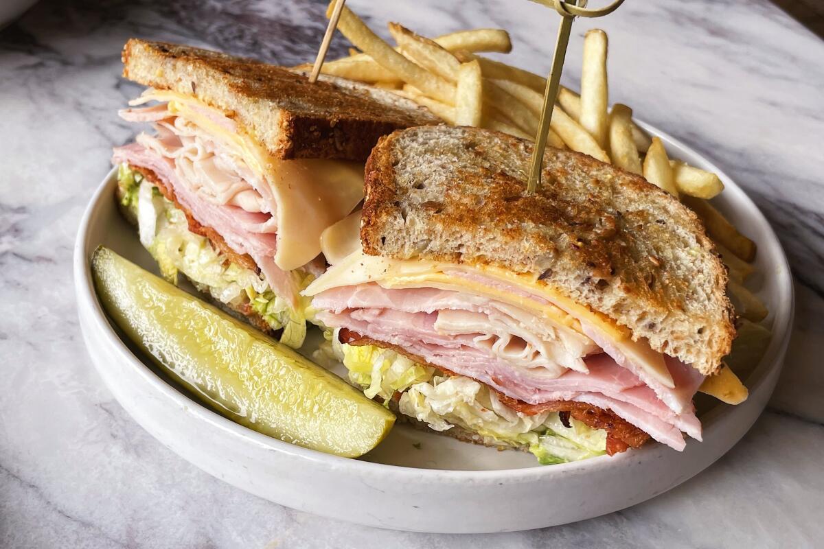 Two halves of a club sandwich with a pickle spear on a marble tabletop at downtown diner Moonlark's Dinette