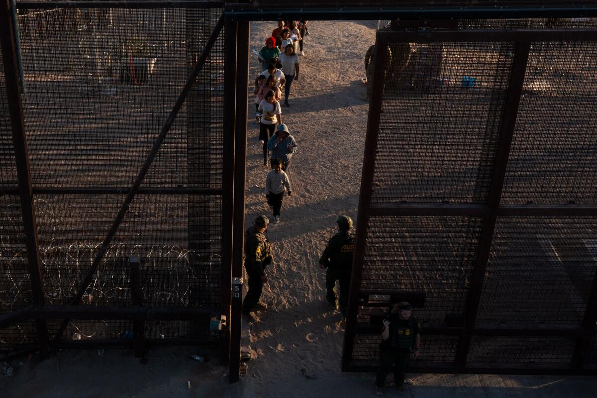 Migrants walk through a gate to board vans after waiting along the border wall