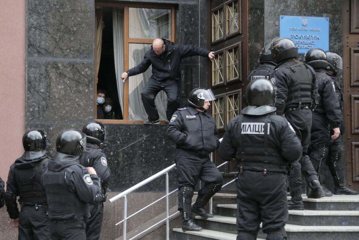 Masked pro-Russian activists look out of a window of the regional prosecutor's office they occupied Saturday as riot police stand nearby in Donetsk, Ukraine. Also Saturday, at least a dozen armed men seized a police station in Slovyansk, a small town about 55 miles south of Donetsk.