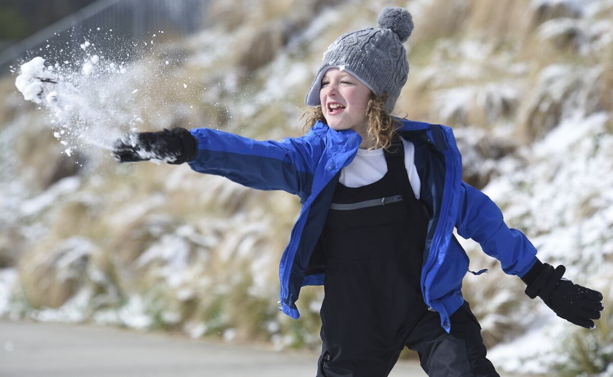 A boy in coat, hat and mittens tosses a handful of snow