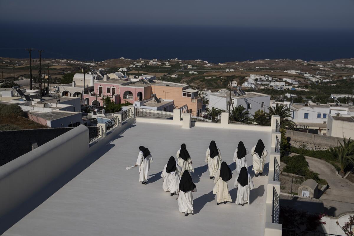 Cloistered nuns walk on a terrace of the Catholic Monastery of St. Catherine on the Greek island of Santorini on Tuesday, June 14, 2022. Twice a day, the nuns recess to chat on the convent's wide terraces, the Aegean Sea shimmering in the distance. (AP Photo/Petros Giannakouris)
