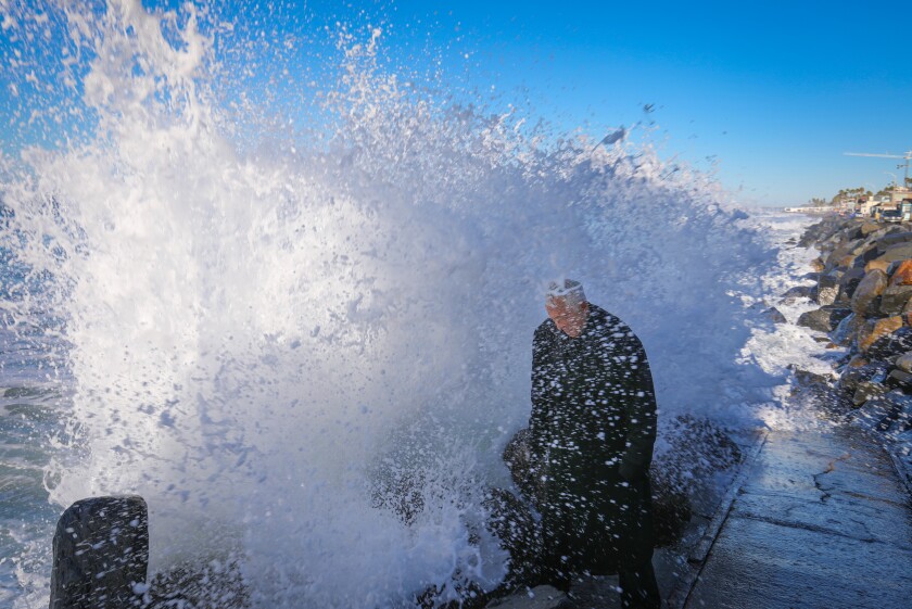 Bruce Parker, known as Oceanside's "Trench Coat Guy," intentionally gets hit with a wave as it crashed over the rocks at the end of Wisconsin Avenue and The Strand on Friday. A regular beach visitor, Parker wears the trench coat as he waits for the waves to hit him. He posts videos of his soggy activities on YouTube.