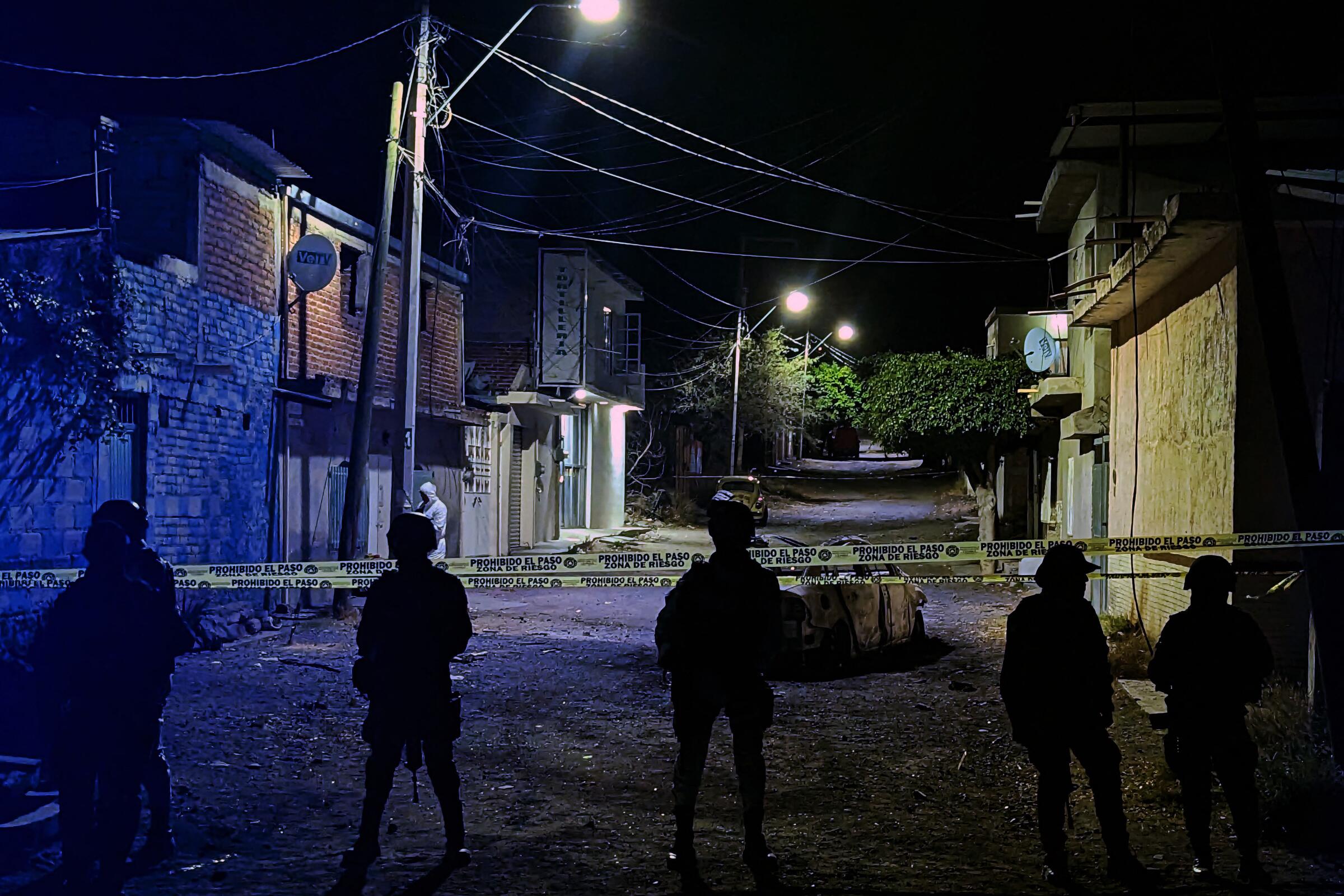 National Guardsmen stand near police tape in a dark street.