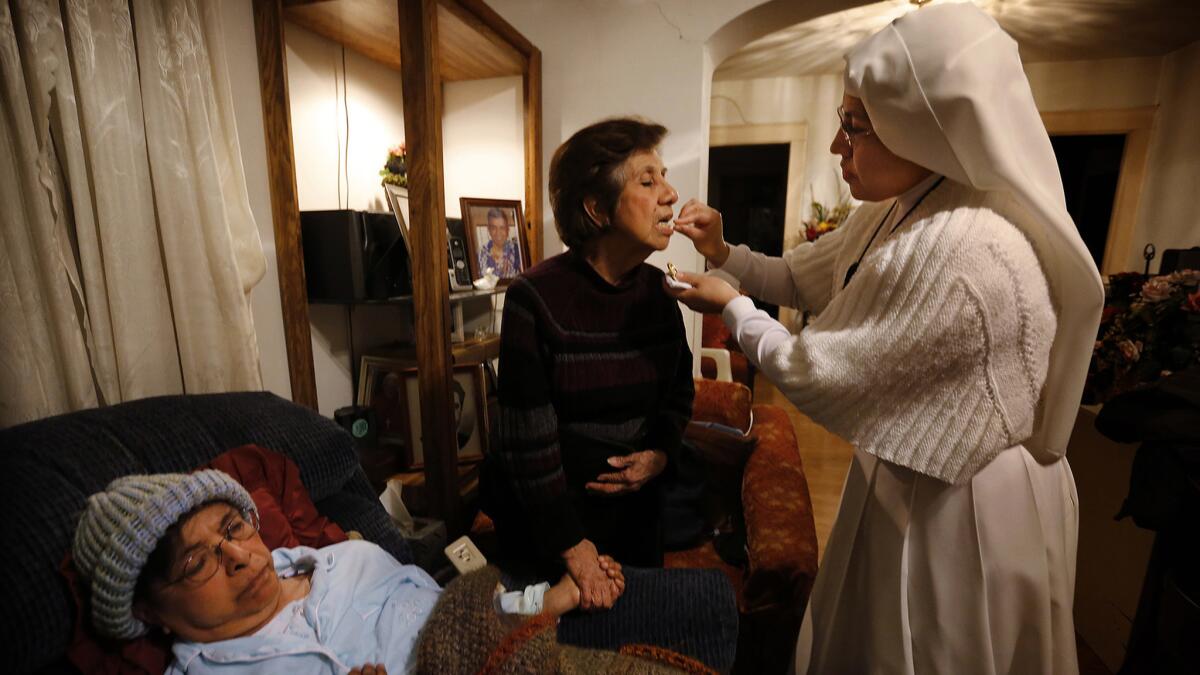 Sister Maria Socorro gives holy communion to Yolanda Calderon at the beside of her sister, Esperanza.