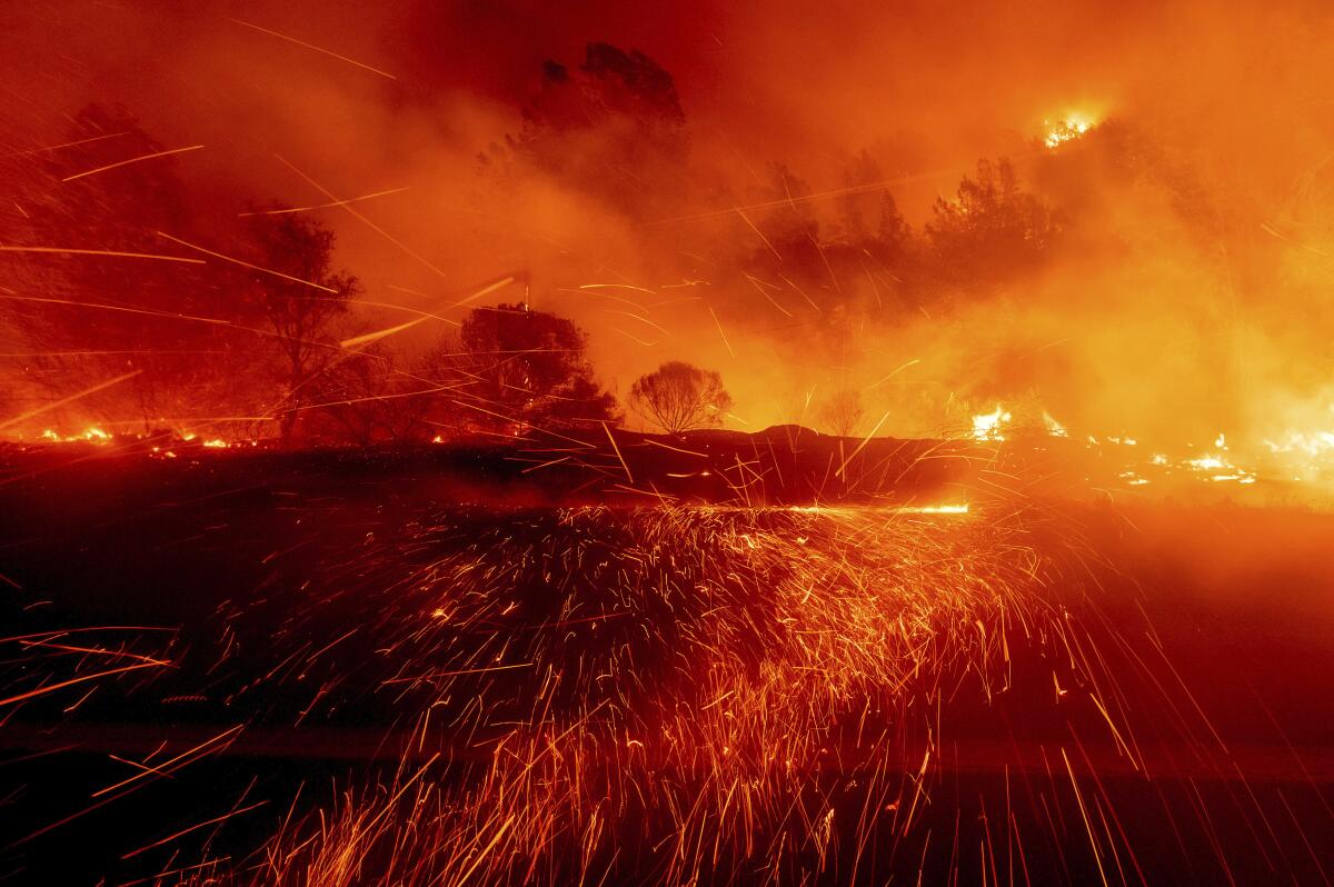 Embers fly across a roadway as flames cast an orange glow